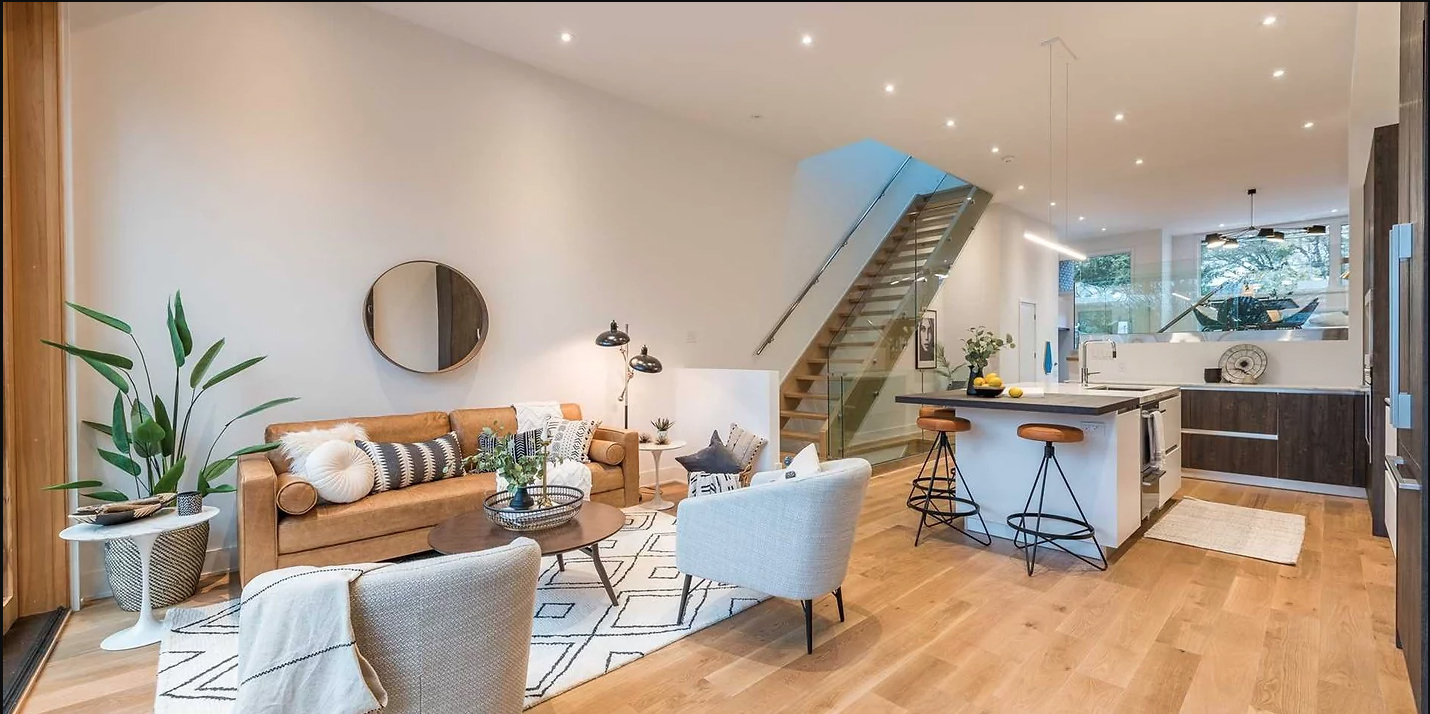 Modern open-concept living space with hardwood floors and glass staircase